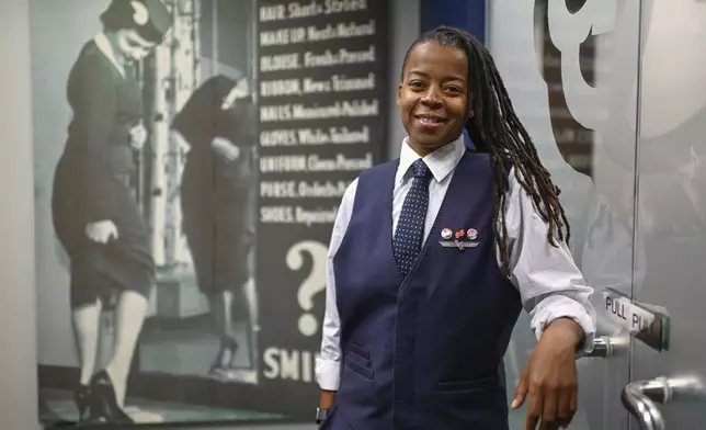 Keturah Johnson, international vice president for flight attendant union AFA-CWA, poses by a decades old, outdated poster with rules and uniforms for flight attendants, at her headquarters office, Wednesday, Sept. 18, 2024, in Washington. (AP Photo/John McDonnell)