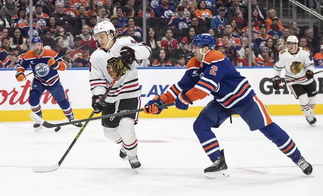 Chicago Blackhawks' Connor Bedard (98) and Edmonton Oilers' Evan Bouchard (2) battle for the puck during the first period of an NHL hockey game, Saturday, Oct. 12, 2024 in Edmonton, Alberta. (Jason Franson/The Canadian Press via AP)