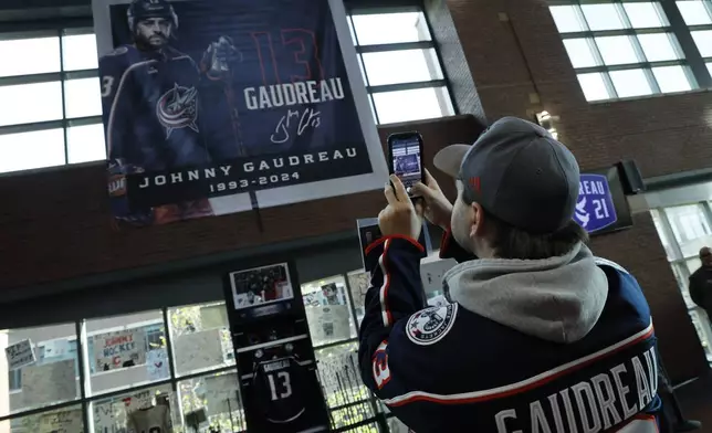 Troy Ward, of Dayton, takes photos of a memorial of Columbus Blue Jackets' Johnny Gaudreau and his brother Matthew before the start of an NHL hockey game against the Florida Panthers. Tuesday, Oct. 15, 2024, in Columbus, Ohio. (AP Photo/Jay LaPrete)