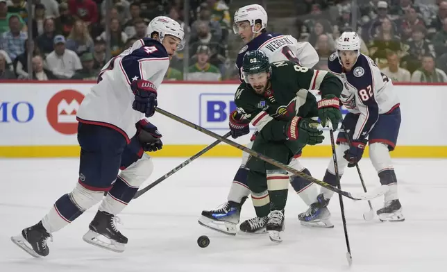 Columbus Blue Jackets center Cole Sillinger, left, and Minnesota Wild center Frederick Gaudreau, center, follow the puck during the first period of an NHL hockey game, Thursday, Oct. 10, 2024, in St. Paul, Minn. (AP Photo/Abbie Parr)