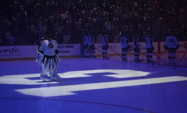 Columbus Blue Jackets goaltender Elvis Merzlikins (90) stands on a No. 13 on the ice honoring former Blue Jackets player Johnny Gaudreau and his brother Matthew Gaudreau who were killed by a driver in New Jersey in August, before an NHL hockey game against the Minnesota Wild, Thursday, Oct. 10, 2024, in St. Paul, Minn. (AP Photo/Abbie Parr)