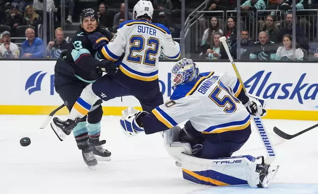 St. Louis Blues goaltender Jordan Binnington (50) looks on as the puck flies out of reach and defenseman Ryan Suter (22) and Seattle Kraken left wing Brandon Tanev, left, collide during the second period of an NHL hockey game Tuesday, Oct. 8, 2024, in Seattle. (AP Photo/Lindsey Wasson)