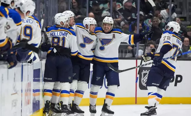 St. Louis Blues center Dylan Holloway (81) hugs defenseman Philip Broberg to celebrate Broberg's goal as defenseman Justin Faulk (72) and center Robert Thomas, second from left, join them to celebrate during the second period of an NHL hockey game against the Seattle Kraken, Tuesday, Oct. 8, 2024, in Seattle. (AP Photo/Lindsey Wasson)