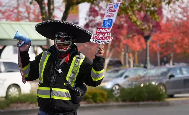 Boeing mechanic Eugenio, who preferred not to give a last name, sounds a bullhorn while holding a sign as employees gather to vote on a new contract offer from the company, Wednesday, Oct. 23, 2024, in Everett, Wash. (AP Photo/Lindsey Wasson)