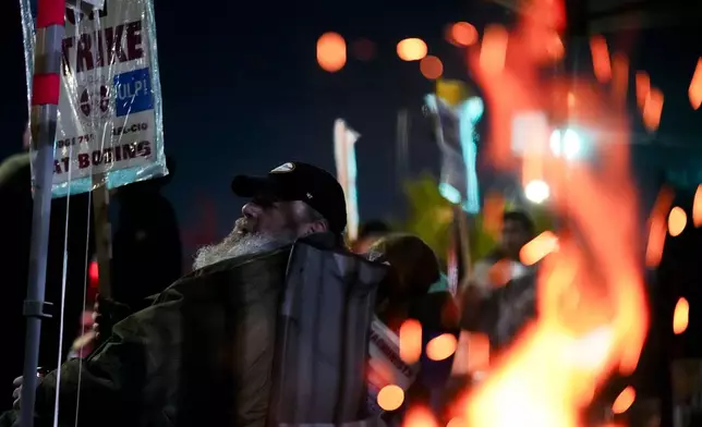 Bryan Osmundson, who has worked for Boeing for 24 years, sits with a picket sign near a burn barrel after union members voted to reject a new contract offer from the company, Wednesday, Oct. 23, 2024, in Renton, Wash. (AP Photo/Lindsey Wasson)