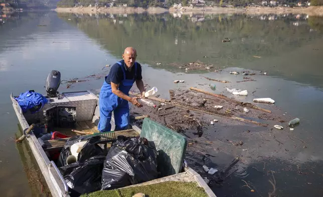 Ibro Mesic collects plastic waste from his boat after devastating floods and landslides that put tons of waste in Jablanicko lake near Ostrozac, Bosnia, Sunday, Oct. 20, 2024. (AP Photo/Armin Durgut)