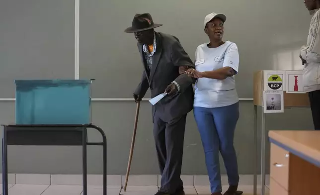 A man assisted by an electoral worker, walks towards the ballot box to cast his vote during the elections in Gaborone, Botswana, Wednesday, Oct. 30, 2024. (AP Photo/Themba Hadebe)