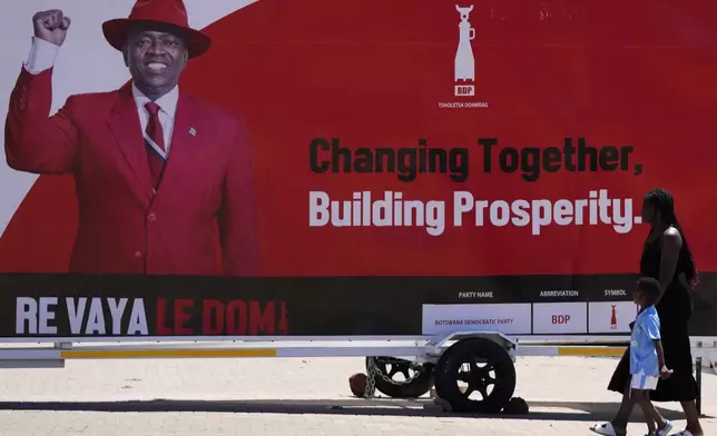 A woman and a child passes an election poster of ruling party Botswana Democratic Party president Mokgweetsi Masisi in Gaborone, Botswana, Tuesday, Oct. 29, 2024. (AP Photo/Themba Hadebe)