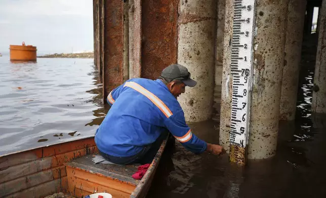 Dock worker Francisco Ferreira Pinheiro reads a meter stick in the Negro River at the port in Manaus, Amazonas state, Brazil, Friday, Oct. 4, 2024, amid a severe drought. (AP Photo/Edmar Barros)