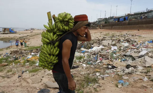 A porter carries bananas brought by boat across a dry area of the Negro River at the port in Manaus, Amazonas state, Brazil, Friday, Oct. 4, 2024, amid a severe drought. (AP Photo/Edmar Barros)