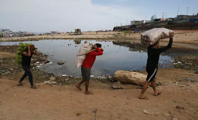 Porters carry goods brought by boat across a dry area of the Negro River at the port in Manaus, Amazonas state, Brazil, Friday, Oct. 4, 2024, amid a severe drought. (AP Photo/Edmar Barros)