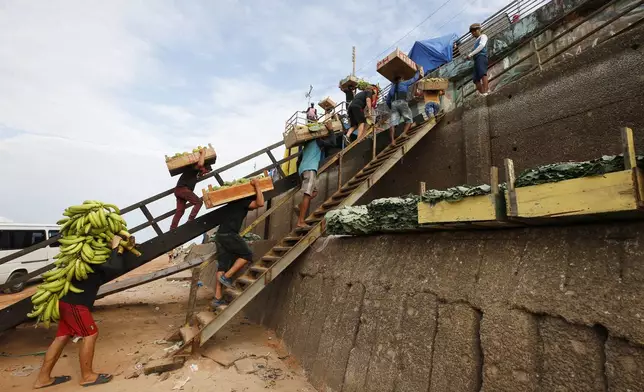 Porters carry goods that arrived by boat up stairs on the bank of the Negro River at the port of Manaus, Amazonas state, Brazil, Friday, Oct. 4, 2024, amid a severe drought. (AP Photo/Edmar Barros)