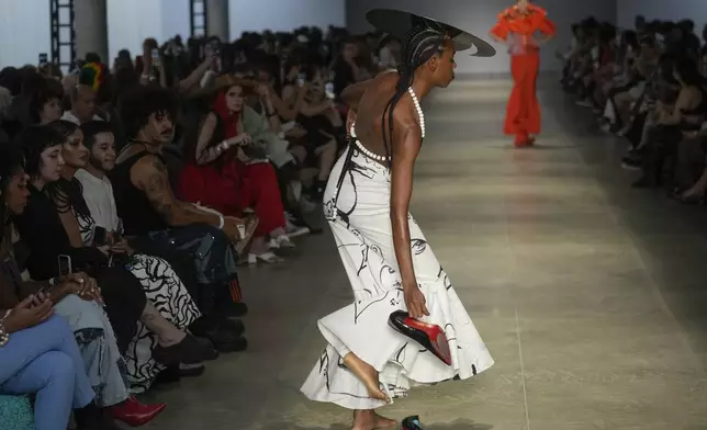 A model takes off her shoes while on the catwalk during the presentation of the Cria Costura collection at Sao Paulo Fashion Week in Sao Paulo, Thursday, Oct. 17, 2024. (AP Photo/Andre Penner)