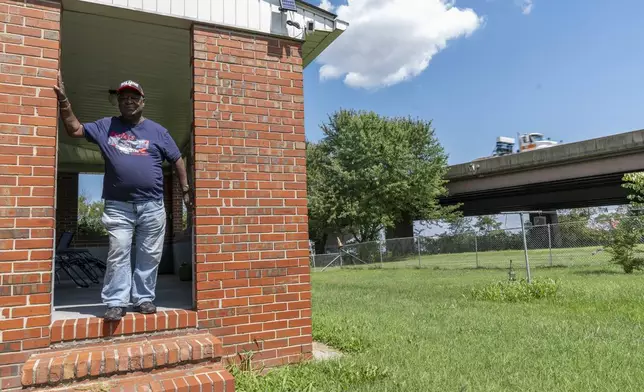 Linwood Jackson poses for a portrait outside of his home, Tuesday, Aug. 13, 2024, as a semi truck drives past on the remaining portion of the Francis Scott Key Bridge in Turner Station, Md. (AP Photo/Stephanie Scarbrough)