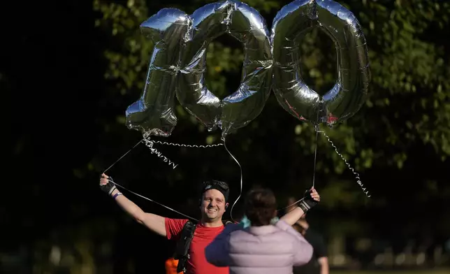 Paul Hoover holds balloons as he poses for a photo before taking part in his 100th parkrun event in Bushy Park, southwest London, Saturday, Sept. 28, 2024. (AP Photo/Alastair Grant)