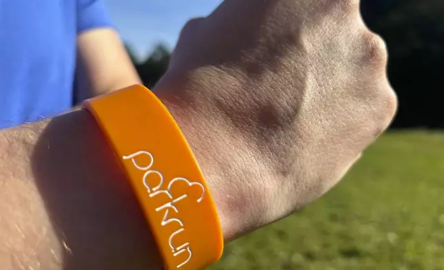 A runner shows off a parkrun wrist band after completing the 5 kilometer (3.1 mile) route in Hampstead Heath in north London on Saturday Sept. 14, 2024. (AP Photo/Lucy Nicholson)