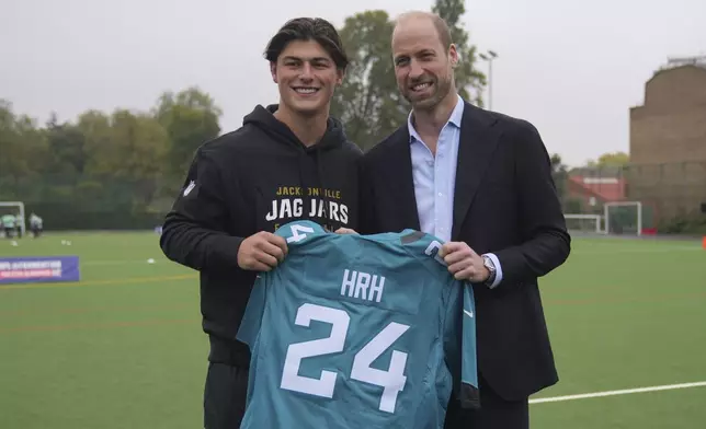 Britain's Prince William, right, poses with Louis Rees-Zammit, holding a NFL shirt as he attends a NFL Foundation NFL Flag event, an inclusive and fast paced American Football format, in London, Tuesday, Oct. 15, 2024. (AP Photo/Kin Cheung, Pool)