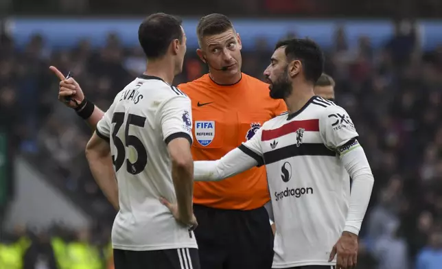 Referee Robert Jones, center, speaks with Manchester United's Jonny Evans, left, and Manchester United's Bruno Fernandes during the English Premier League soccer match between Aston Villa and Manchester United, at Villa Park in Birmingham, England, Sunday, Oct. 6, 2024. (AP Photo/Rui Vieira)