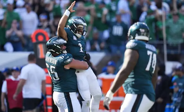 Philadelphia Eagles quarterback Jalen Hurts (1) is lifted by Eagles offensive tackle Lane Johnson (65) after Hurts threw a touchdown pass to Eagles wide receiver DeVonta Smith during the second half of an NFL football game against the Cleveland Browns on Sunday, Oct. 13, 2024, in Philadelphia. (AP Photo/Chris Szagola)