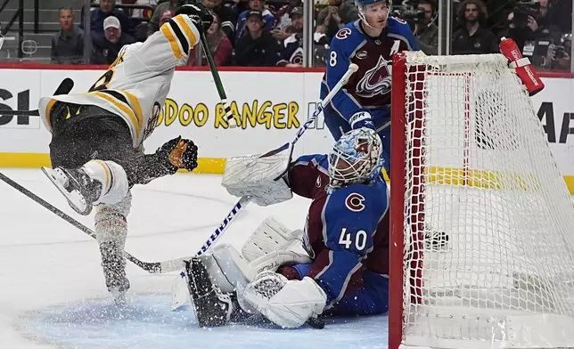 Boston Bruins right wing David Pastrnak, left, flies through the air after scoring a goal on Colorado Avalanche goaltender Alexandar Georgiev in the second period of an NHL hockey game Wednesay, Oct. 16, 2024, in Denver. (AP Photo/David Zalubowski)