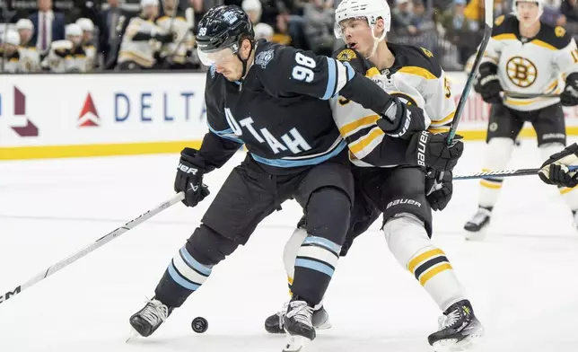 Utah Hockey Club defenseman Mikhail Sergachev (98) and Boston Bruins center Morgan Geekie compete for the puck during the third period of an NHL hockey game, Saturday, Oct. 19, 2024, in Salt Lake City. (AP Photo/Spenser Heaps)