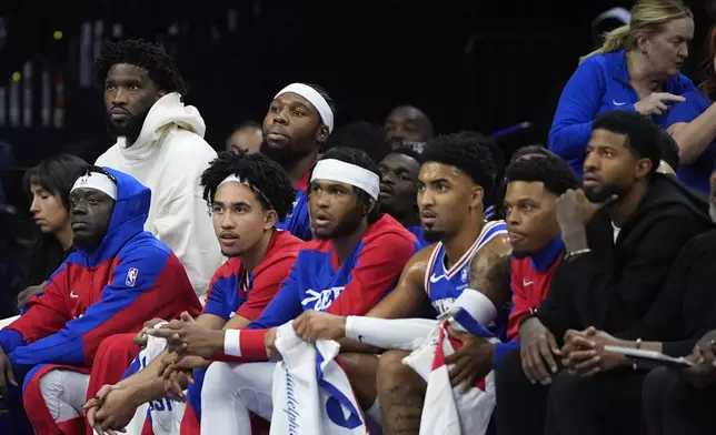 Philadelphia 76ers' Joel Embiid, top left, and Paul George, bottom right, watch from the bench during the first half of an NBA basketball game against the Milwaukee Bucks, Wednesday, Oct. 23, 2024, in Philadelphia. (AP Photo/Matt Slocum)