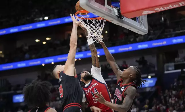 New Orleans Pelicans forward Brandon Ingram (14) goes to the basket between Chicago Bulls center Nikola Vucevic (9) and guard Ayo Dosunmu (11) in the first half of an NBA basketball game in New Orleans, Wednesday, Oct. 23, 2024. (AP Photo/Gerald Herbert)