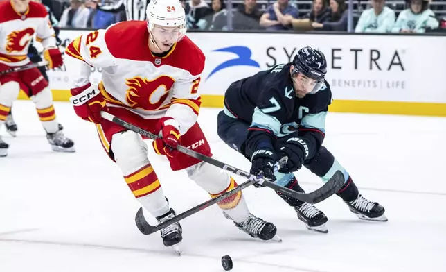 CORRECTS CAPTION TO SECOND PERIOD FROM THIRD PERIOD - Calgary Flames defenseman Jake Bean, left, and Seattle Kraken forward Jordan Eberle battle for the puck during the second period of an NHL hockey game, Saturday, Oct. 19, 2024, in Seattle. (AP Photo/Stephen Brashear)