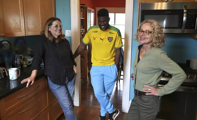 CORRECTS SPELLING OF LAST NAME Cabrel Ngounou, center, a refugee from Cameroon, talks with his sponsors Lori Ostlund, left, and Anne Raeff in their home in San Francisco, Tuesday, Sept. 17, 2024. (AP Photo/Terry Chea)