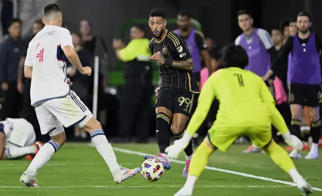 CORRECTS TO SECOND HALF FROM FIRST HALF - Los Angeles FC forward Denis Bouanga (99) kicks the ball between Vancouver Whitecaps defender Ranko Veselinović (4) and goalkeeper Yohei Takaoka (1) during the second half of the first match of an MLS Cup playoffs opening round in Los Angeles, Sunday, Oct. 27, 2024. (AP Photo/Alex Gallardo)