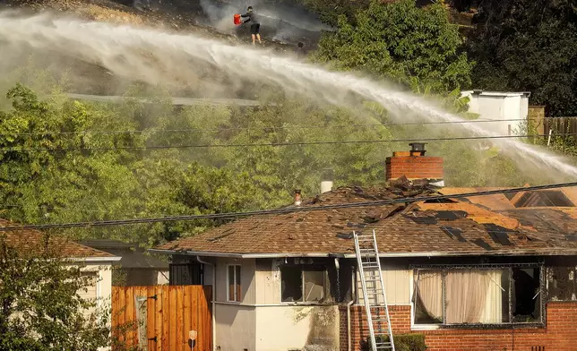 A person dumps water on a grass fire burning above Interstate 580 in Oakland, Calif., Friday, Oct. 18, 2024. (AP Photo/Noah Berger)