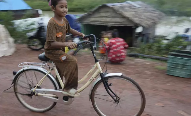 A girl rides a bicycle at a floating village, by the Tonle Sap in Kampong Chhnang province, Cambodia, Thursday, Aug. 1, 2024, (AP Photo/Heng Sinith)