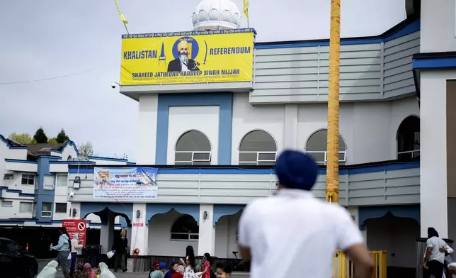 FILE -People sit on the lawn of the the Guru Nanak Sikh Gurdwara, below a picture of Hardeep Singh Nijjar in Surrey, B.C. on Friday, May 3, 2024. (Ethan Cairns/The Canadian Press via AP, File)