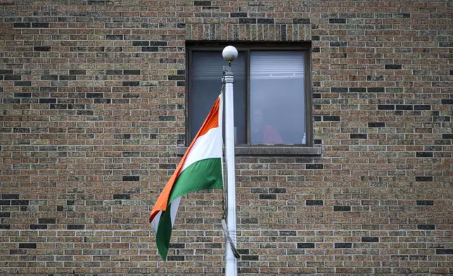 The flag of India flies in front of a person standing at a window, at The High Commission of India in Canada, in Ottawa, Ontario, on Monday, Oct. 14, 2024. (Justin Tang/The Canadian Press via AP)