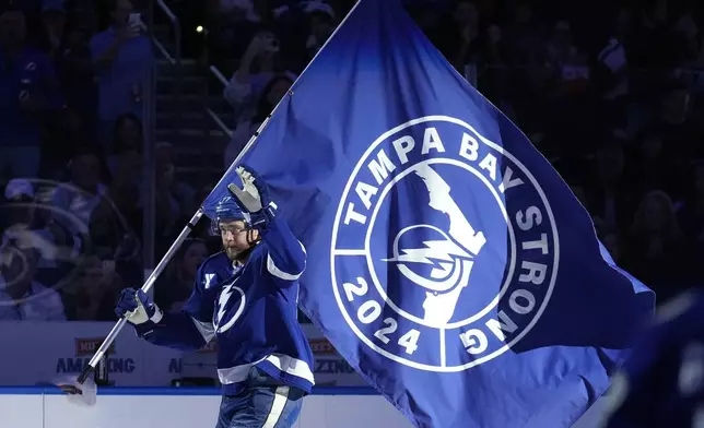 Tampa Bay Lightning defenseman Victor Hedman carries a "Tampa Strong" flag in honor of the victims of Hurricane Milton before an NHL hockey game against the Vancouver Canucks Tuesday, Oct. 15, 2024, in Tampa, Fla. (AP Photo/Chris O'Meara)