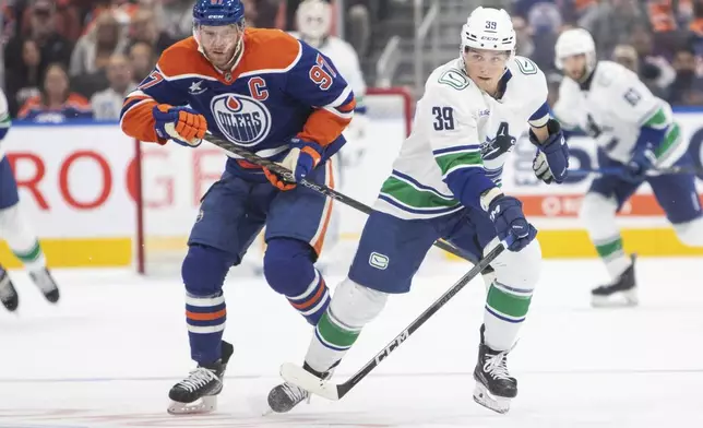 Vancouver Canucks' Ty Mueller (39) carries the puck ahead of Edmonton Oilers' Connor McDavid (97) during the third period of a preseason NHL hockey game in Edmonton, Alberta, Monday, Sept. 30, 2024. (Amber Bracken/The Canadian Press via AP)