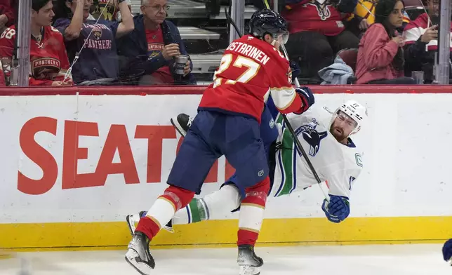 Florida Panthers center Eetu Luostarinen (27) slams Vancouver Canucks defenseman Filip Hronek (17) into the boards during the first period of an NHL hockey game, Thursday, Oct. 17, 2024, in Sunrise, Fla. (AP Photo/Wilfredo Lee)