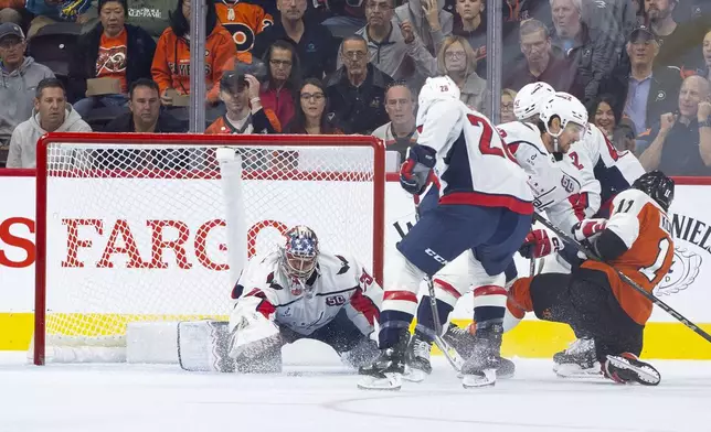 Washington Capitals' Charlie Lindgren, left, reaches for the puck as his teammates keep Philadelphia Flyers' Travis Konecny, right, away from it during the first period of an NHL hockey game, Tuesday, Oct. 22, 2024, in Philadelphia. (AP Photo/Chris Szagola)