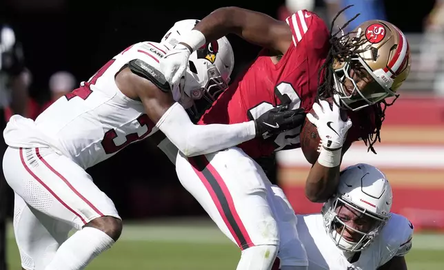 San Francisco 49ers running back Jordan Mason, middle, runs against Arizona Cardinals safety Jalen Thompson, left, and linebacker Jesse Luketa during the second half of an NFL football game in Santa Clara, Calif., Sunday, Oct. 6, 2024. (AP Photo/Godofredo A. Vásquez)