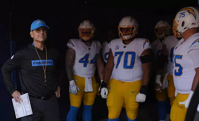 Los Angeles Chargers head coach Jim Harbaugh stands in a tunnel with players before an NFL football game against the Denver Broncos, Sunday, Oct. 13, 2024, in Denver. (AP Photo/David Zalubowski)