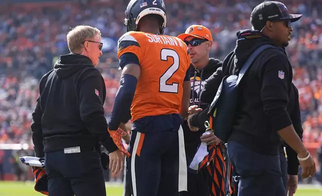 Denver Broncos cornerback Pat Surtain II (2) stands with trainers after sustaining an injury during the first half of an NFL football game against the Los Angeles Chargers, Sunday, Oct. 13, 2024, in Denver. (AP Photo/David Zalubowski)