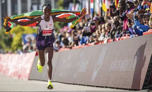 Ruth Chepngetich, from Kenya, runs with the Kenyan flag after crossing the finish line of the Chicago Marathon to win the women's professional division and break the women's marathon world record in Grant Park, Sunday, Oct. 13, 2024. (Tess Crowley/Chicago Tribune via AP)