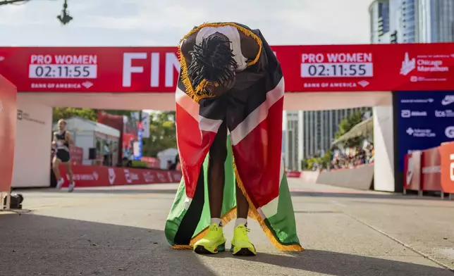 Ruth Chepngetich, from Kenya, lowers her head while wearing the Kenyan flag after crossing the finish line of the Chicago Marathon to win the women's professional division and break the women's marathon world record in Grant Park on Sunday, Oct. 13, 2024. (Tess Crowley/Chicago Tribune via AP)