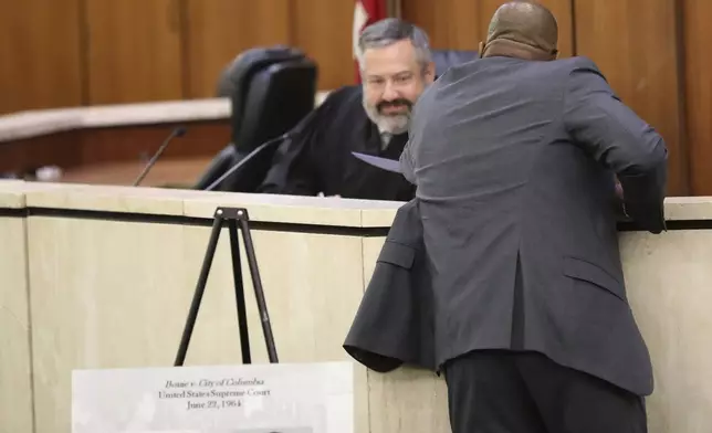 Solicitor Byron Gipson hands up papers clearing the records of seven men arrested in 1960 for sitting at an all-white South Carolina lunch counter to Judge Robert Hood on Friday, Oct. 25, 2024, in Columbia, S.C. (AP Photo/Jeffrey Collins)