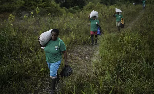 A group of women, part of Asociacion Nuestra Casa Comun, or Our Community House Association, carry a bunch of fertilizer to reforest an area destroyed by illegal mining, near Paimado, Colombia, Tuesday, Sept. 24, 2024. (AP Photo/Ivan Valencia)