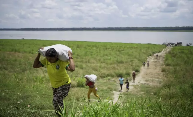 People from the Tikuna Indigenous community carry aid from a nonprofit amid a drought on Amazon River in Loma Linda, near Leticia, Colombia, Sunday, Oct. 20, 2024. (AP Photo/Ivan Valencia)