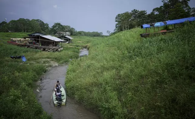 People maneuver by boat through the low level of a tributary that connects with the Amazon River, in Isla de la Fantasia, on the outskirts of Leticia, Colombia, Sunday, Oct. 20, 2024. (AP Photo/Ivan Valencia)