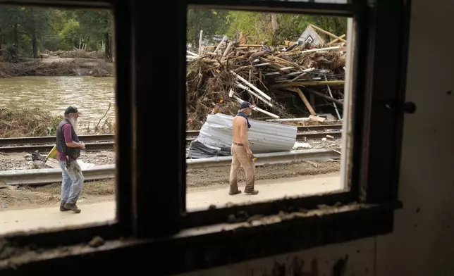 FILE - People walk by a pile of debris left in the wake of Hurricane Helene, Oct. 1, 2024, in Marshall, N.C. (AP Photo/Jeff Roberson, File)