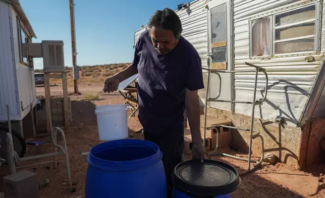 Ricky Gillis collects water for use in a evaporative air cooling unit, at left, Wednesday, Oct. 9, 2024, at his home on the Navajo Nation in Halchita, Utah. (AP Photo/Joshua A. Bickel)