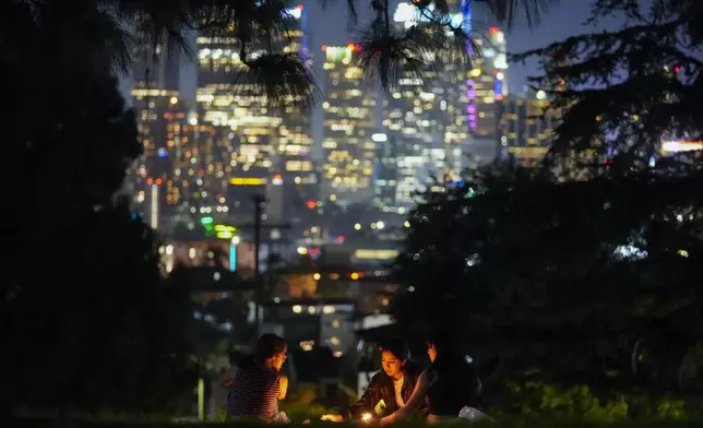 FILE - The downtown Los Angeles skyline gives a backdrop to artists painting under candlelight at Everett Triangle Park, Oct. 22, 2024, in Los Angeles. (AP Photo/Julio Cortez, File)